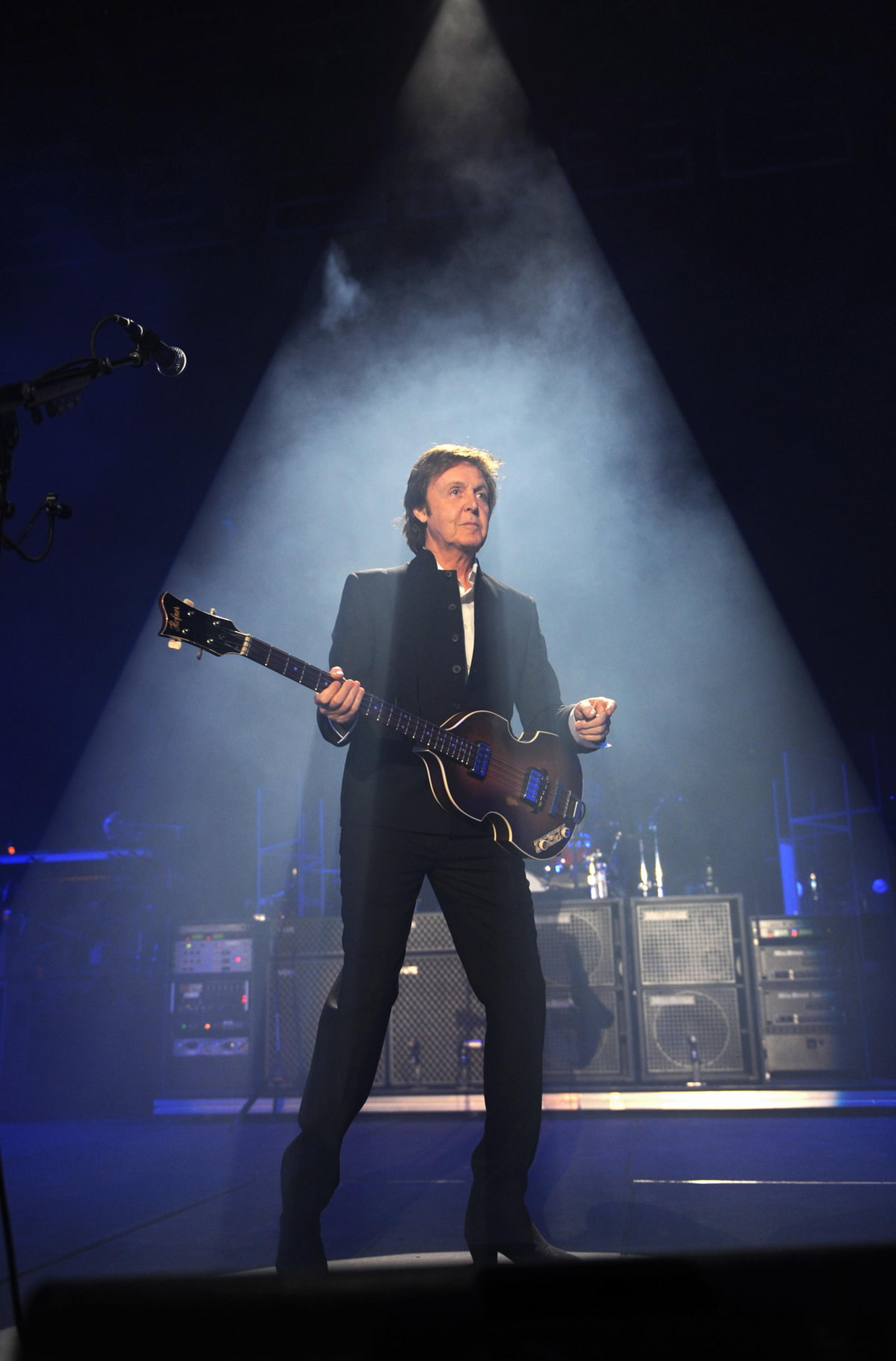 Paul stands on stage in a blue light, holding a bass guitar