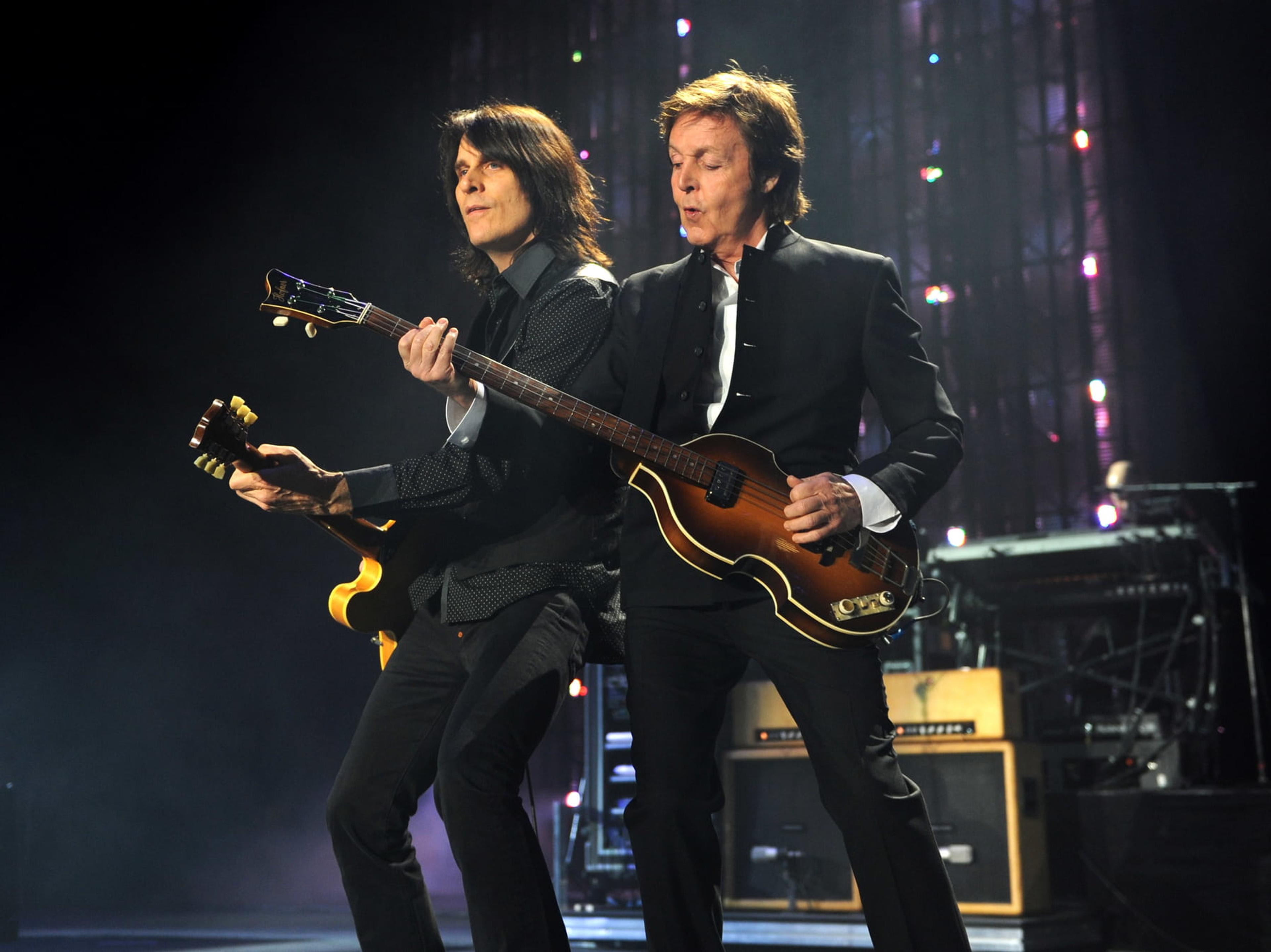 Paul stands on stage with his guitar and guitarist