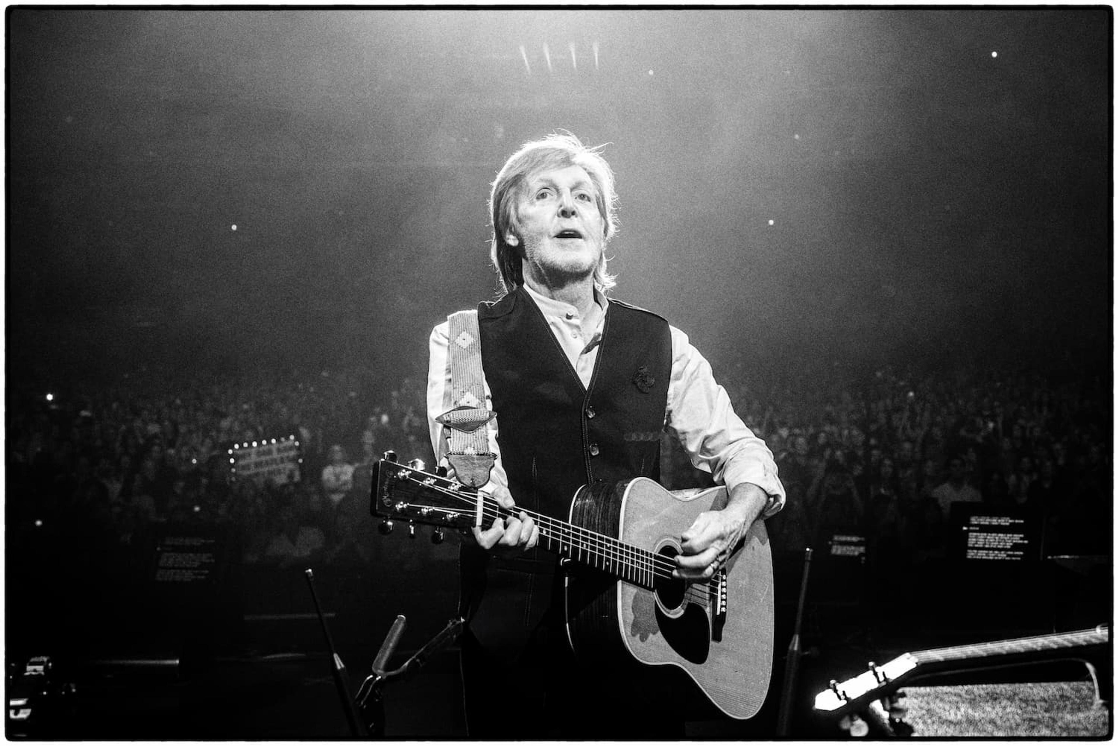 Black and white photo of Paul performing with an acoustic guitar on stage at the BOK Center in Tulsa, 2025, with stage lighting highlighting his silhouette. Photo by MJ Kim.