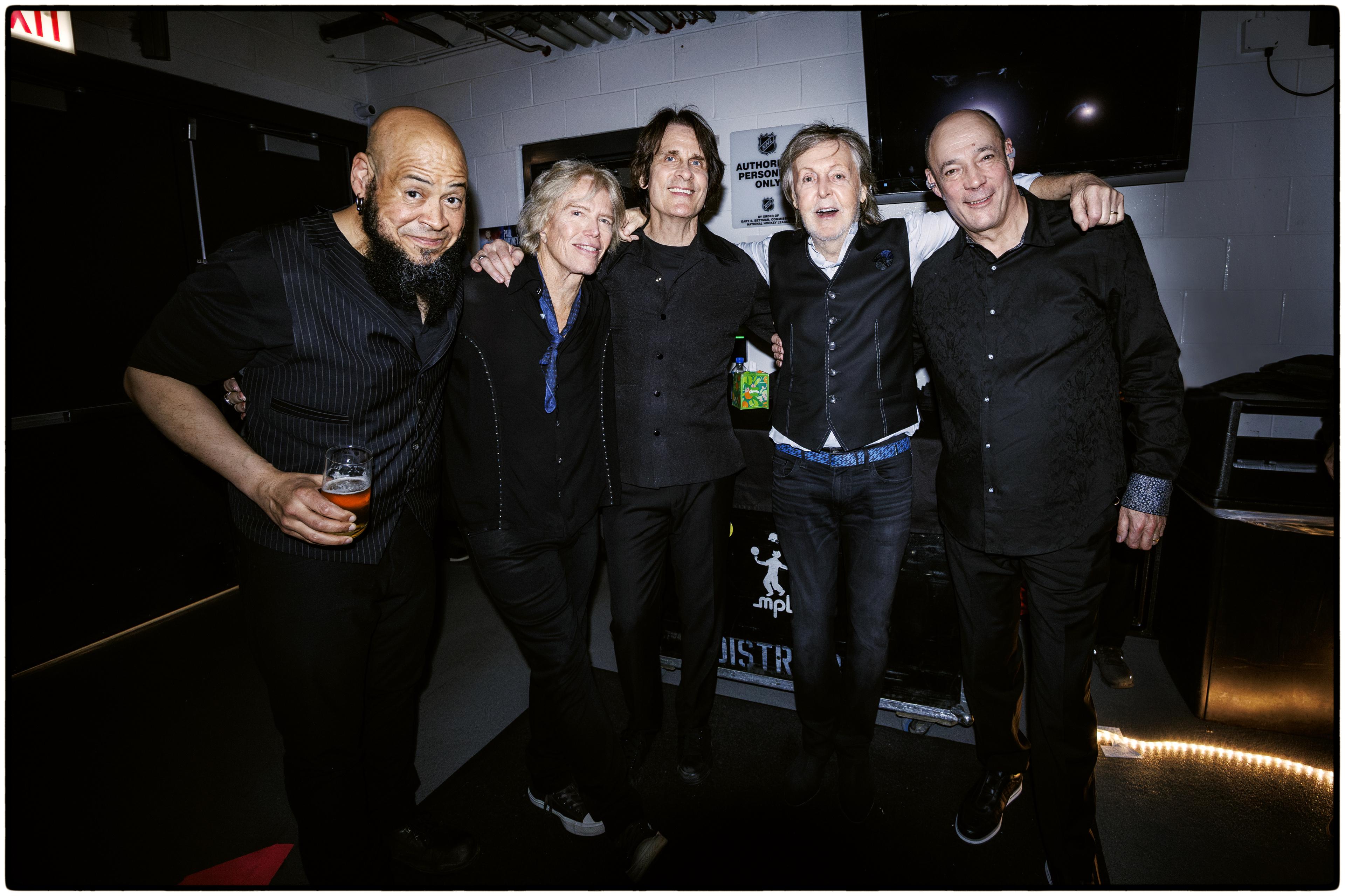 Colour photograph of Paul backstage with his band, featuring from left to right: Abe Laboriel Jr., Brian Ray, Rusty Anderson, Paul McCartney and Paul “Wix” Wickens.