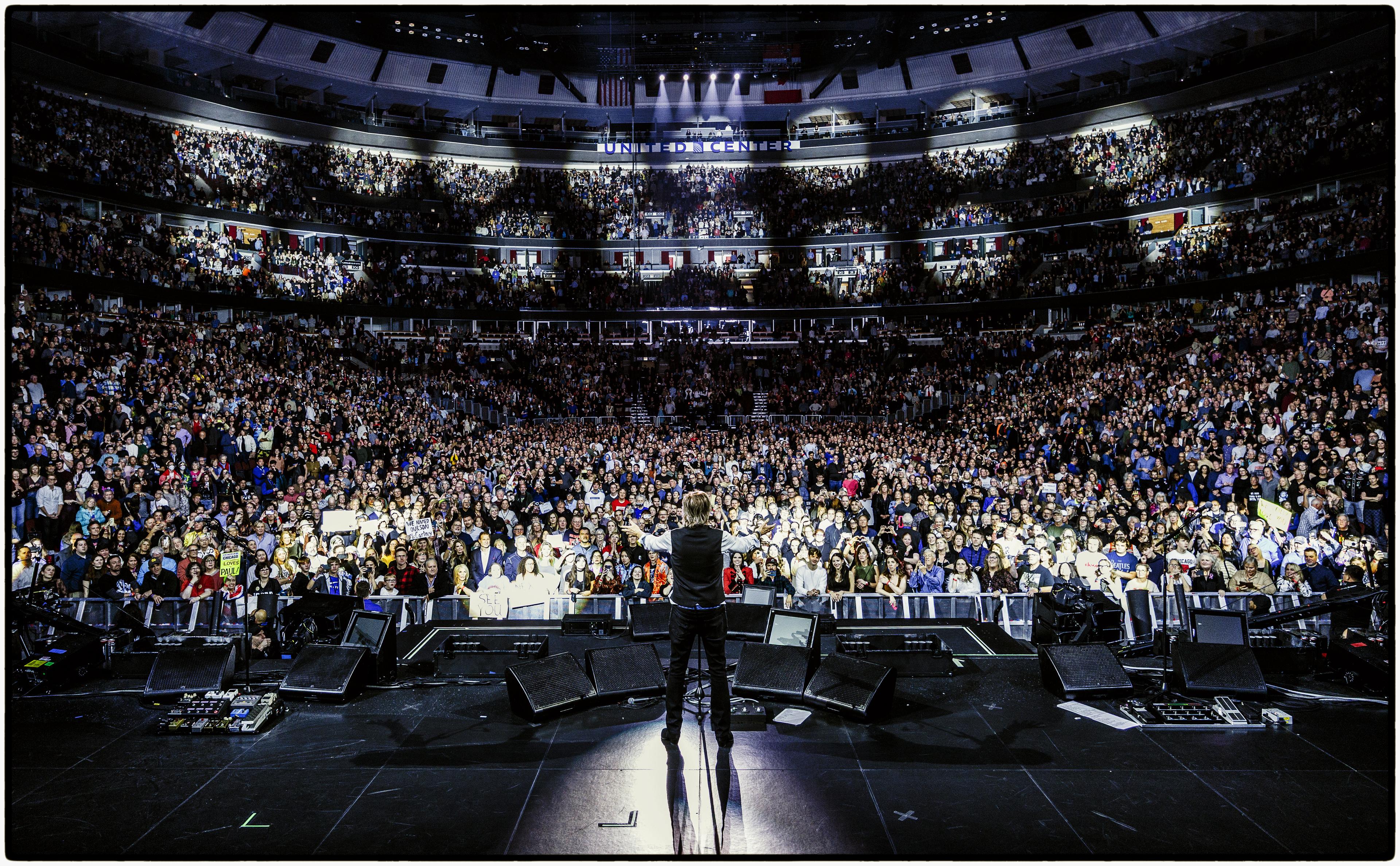 Photo of Paul taken from behind as he performs on stage at Chicago’s sold‑out United Center, looking out toward the arena crowd