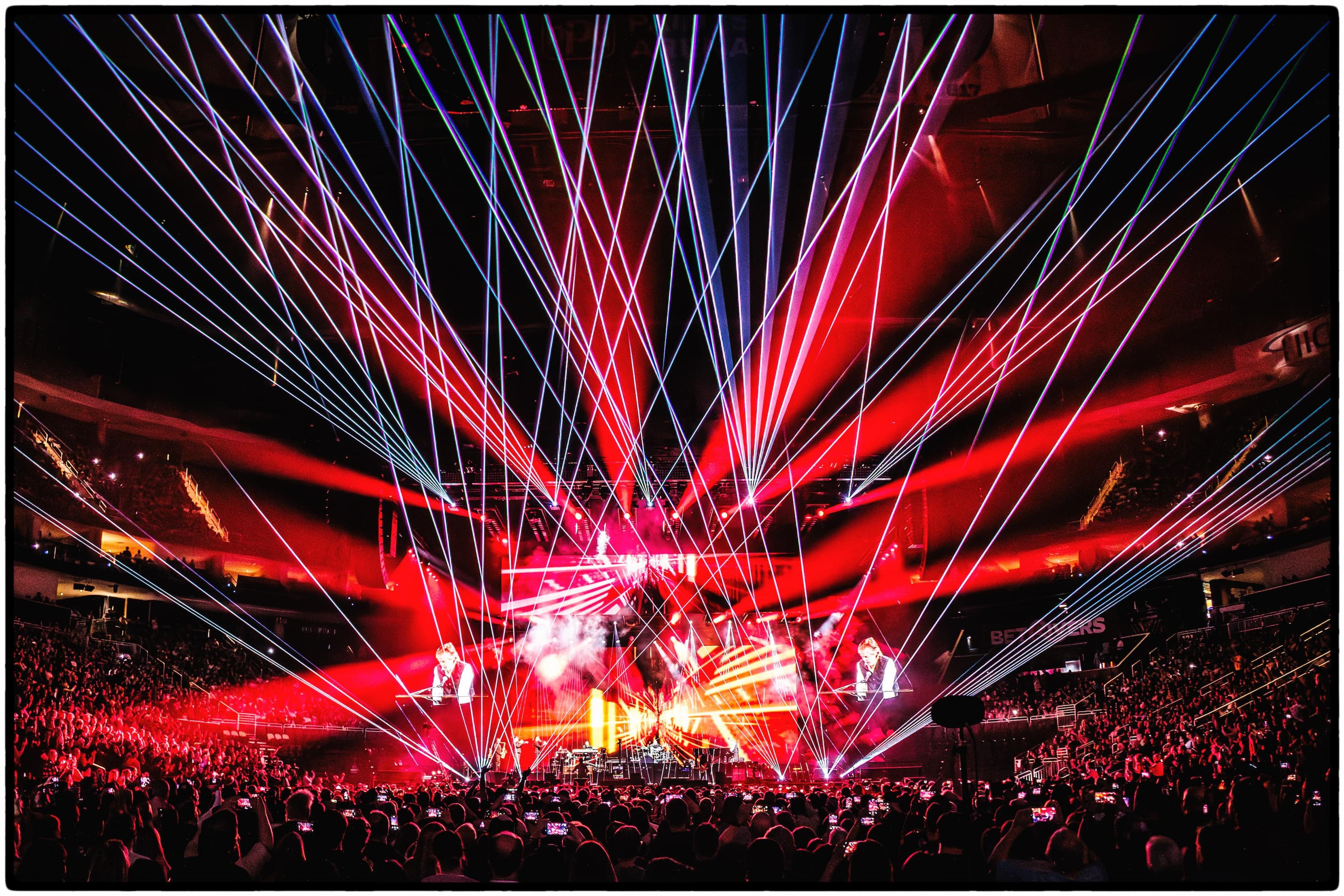 Photo of Paul McCartney performing on stage at Pittsburgh’s PPG Paints Arena, with colorful lasers and bright stage lights illuminating the scene.
