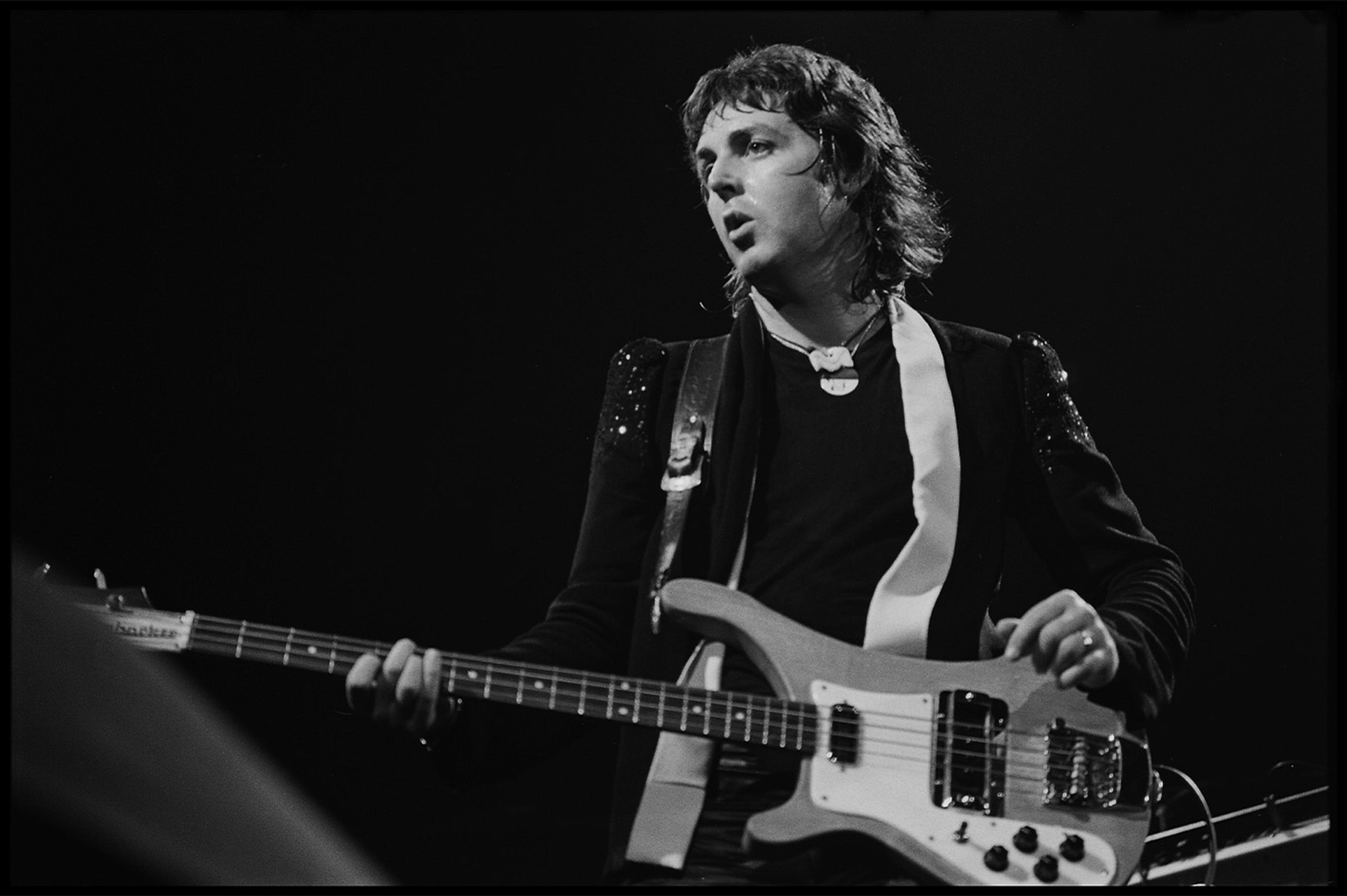 Black and white photograph of Paul McCartney playing the bass on stage during the Wings period