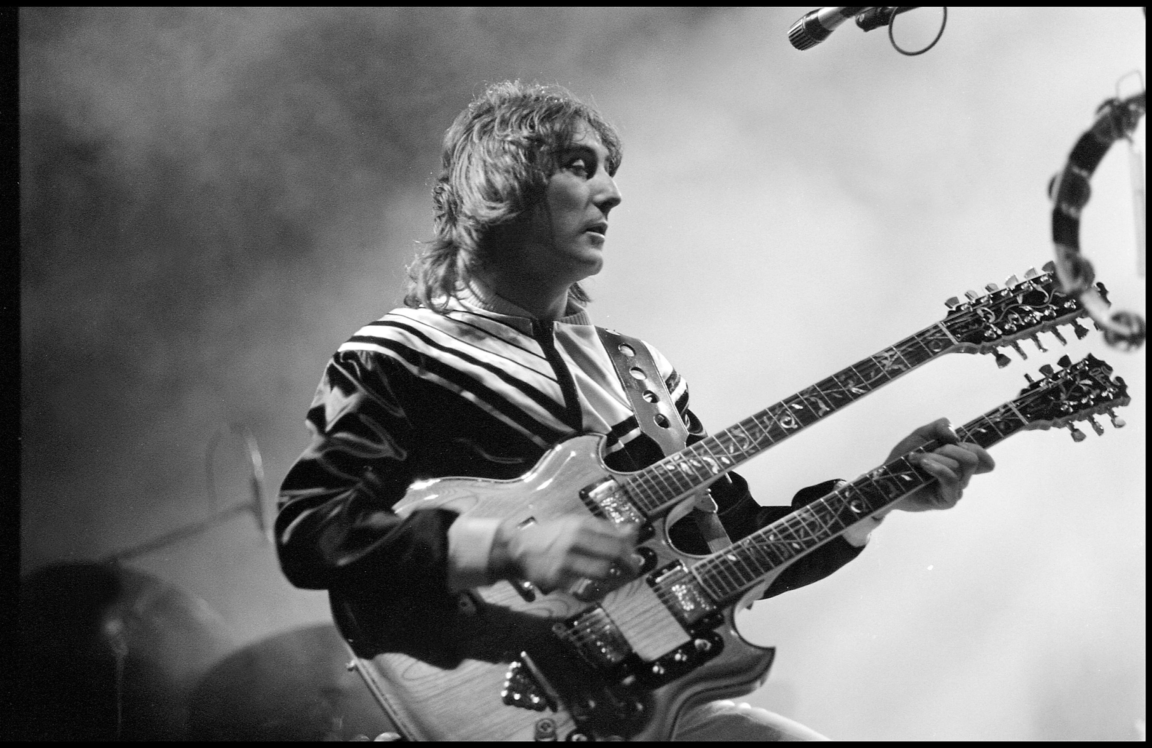 Black and white photograph of Denny Laine playing a two headed guitar on stage
