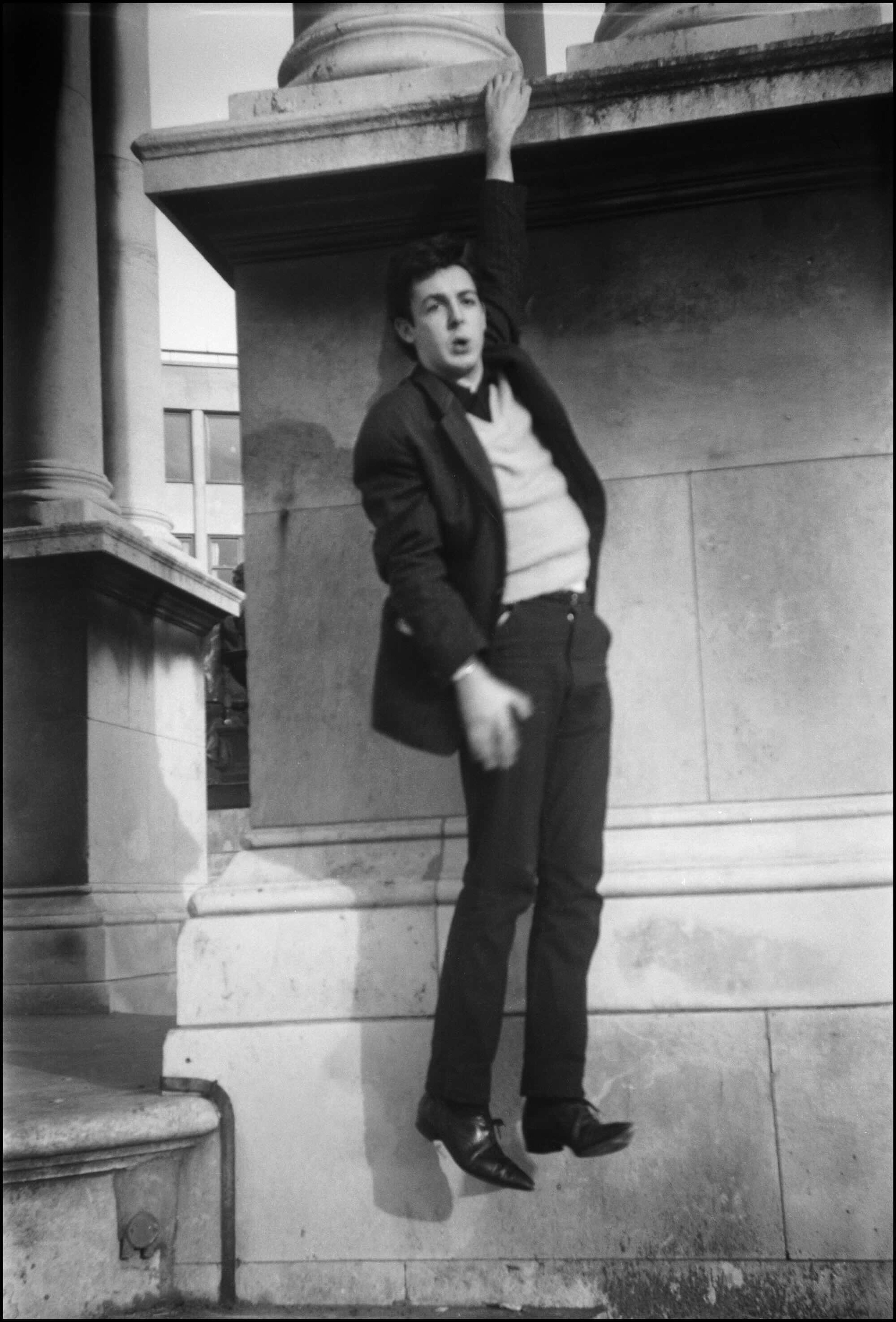 Black and White photo of a young Paul McCartney hanging off Victoria Monument in Liverpool