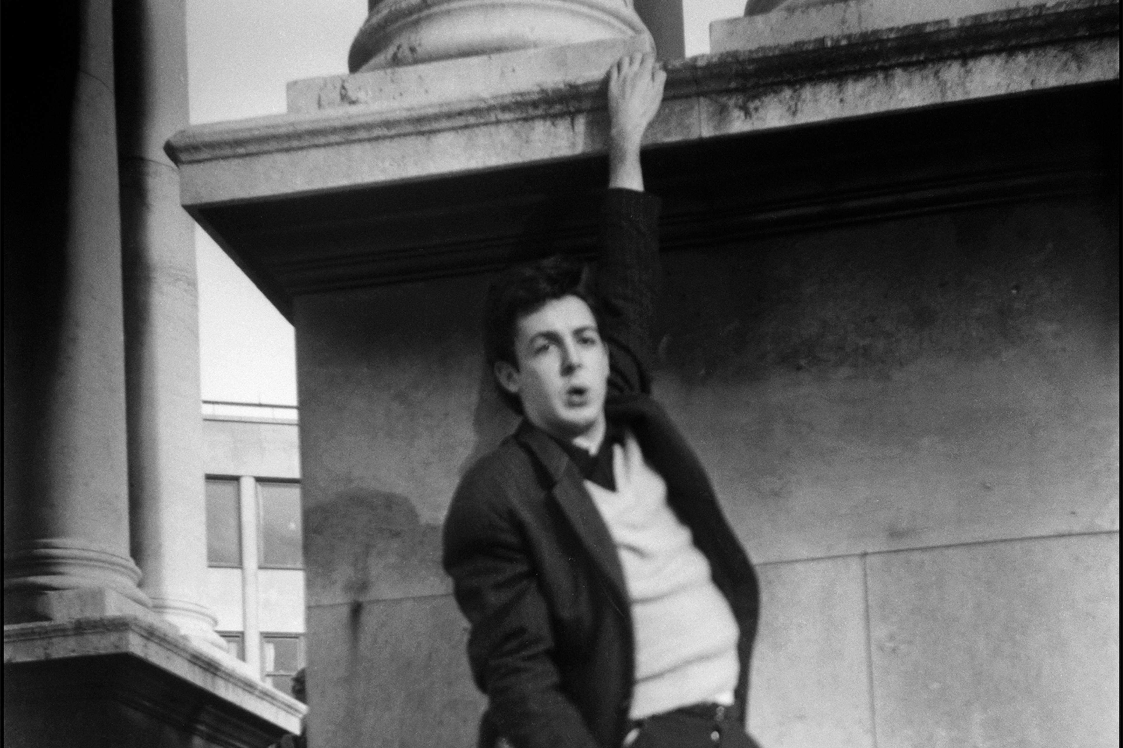 Black and White photo of a young Paul McCartney hanging off Victoria Monument in Liverpool