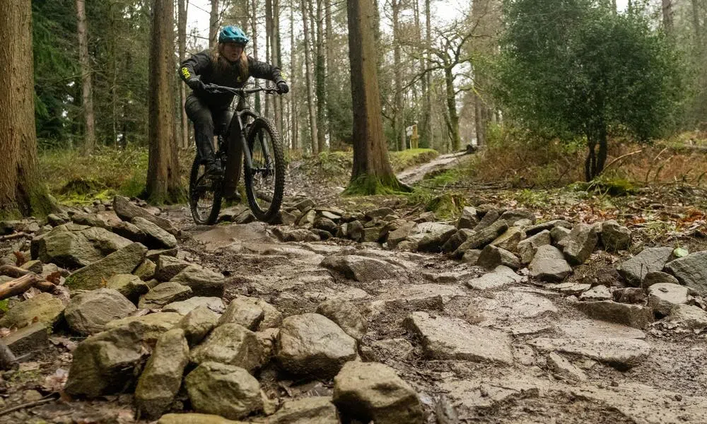 mountain biker riding over rocky terrain in the woods in wet conditions