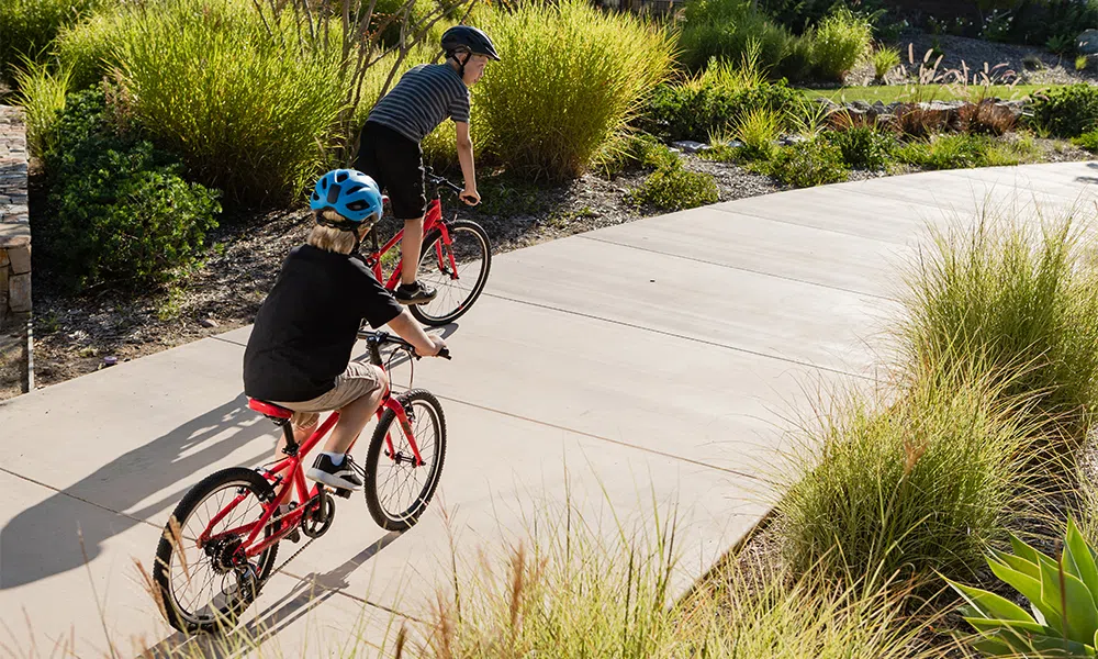 Two kids ride bikes together on a path 