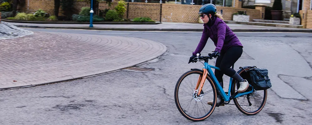 A woman rides a blue electric urban bikes around a roundabout