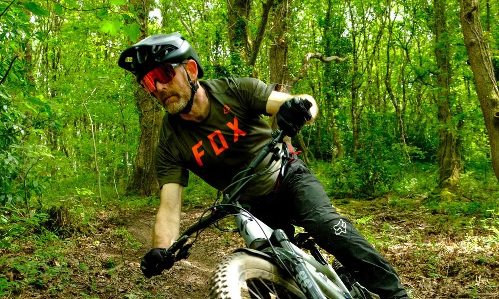 Mountain biker riding in the woods wearing Smith sunglasses and a Fox clothing top