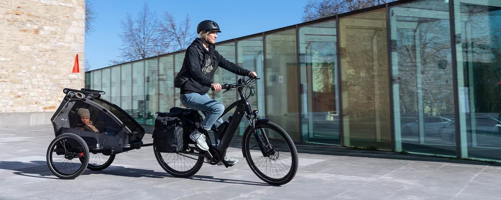 woman towing a child in a child trailer with an e-bike