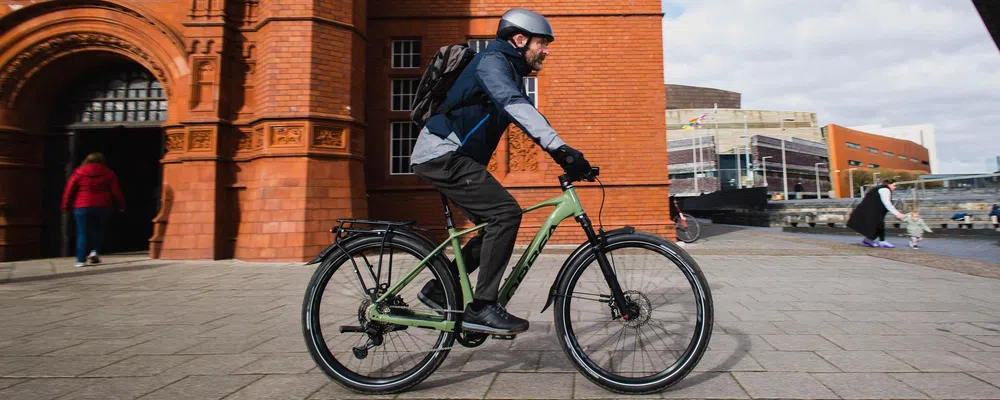 man cycling past red brick building on an e-bike