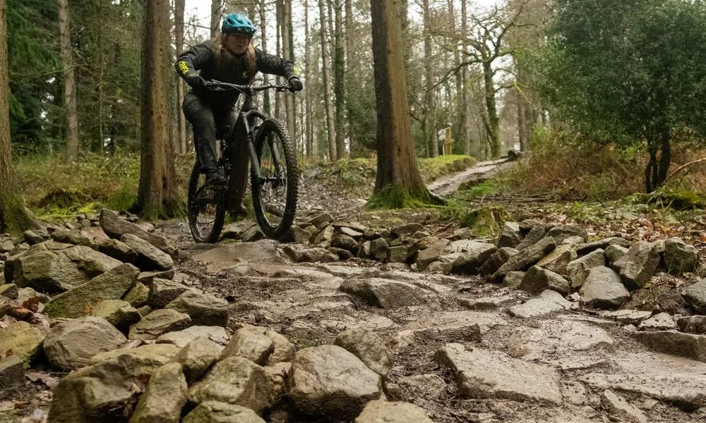 mountain bike rider cycling through a rock garden on a wet muddy day