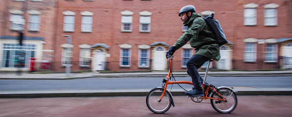 a folding brompton bike is ridden past a red brick building