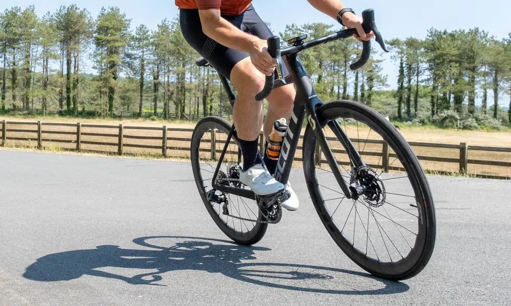 Close up of a Scott road bike being ridden on a summer day with shadow