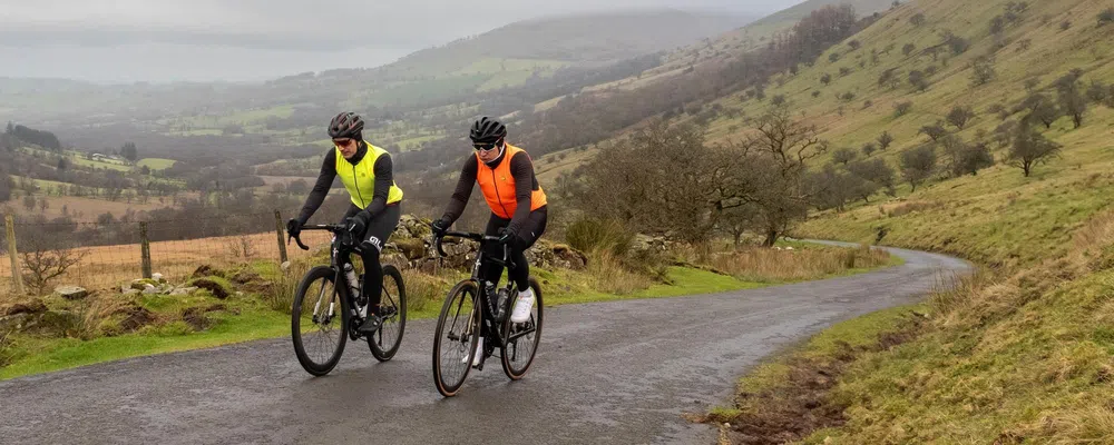 Tow road cyclists climbing in the Welsh hills on a cold winter day wearing Ale kit including Gilets