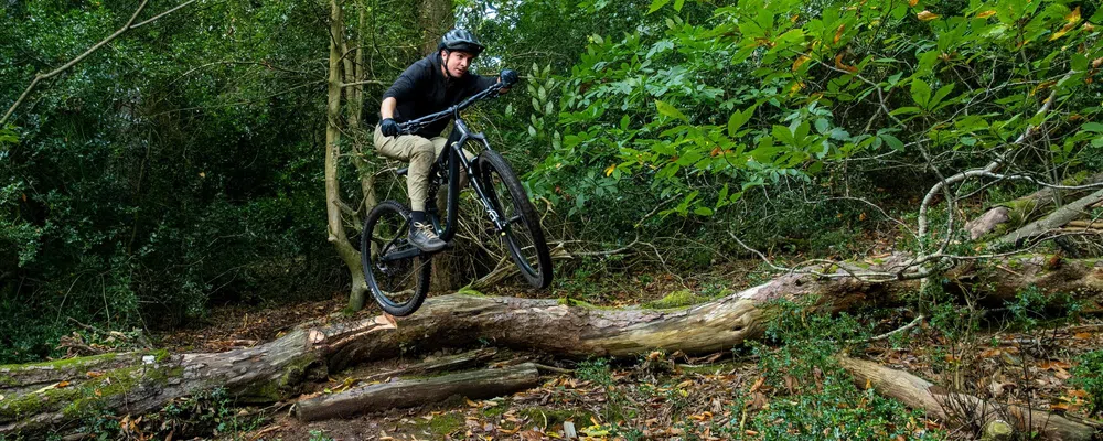 Riding a mountain bike in the woods, man jumping over a log