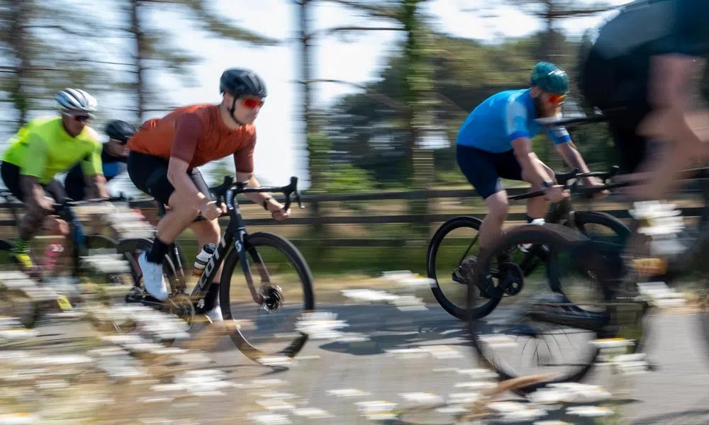 Pan shot, road cyclists riding fast in a group on a sunny day with flowers 