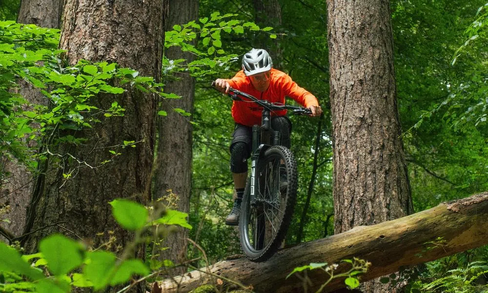 mountain biker off drop in silver tld helmet and orange Merida top 