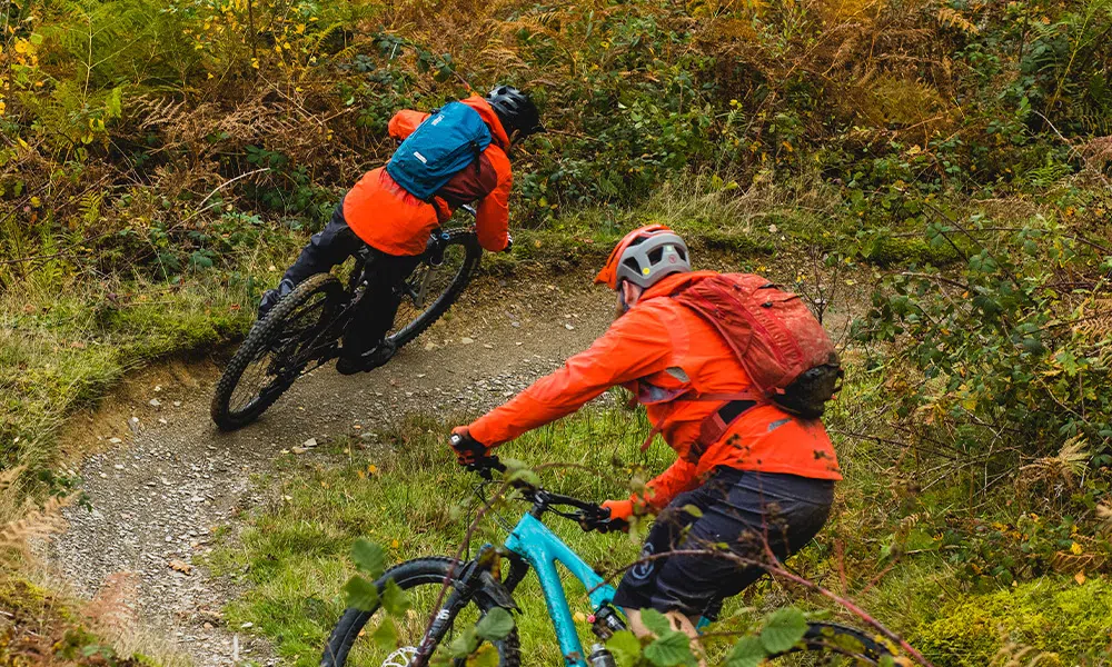 2 mountain bikers riding a berm with winter clothes and bags