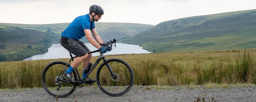 a gravel bike rides past a reservoir and hills