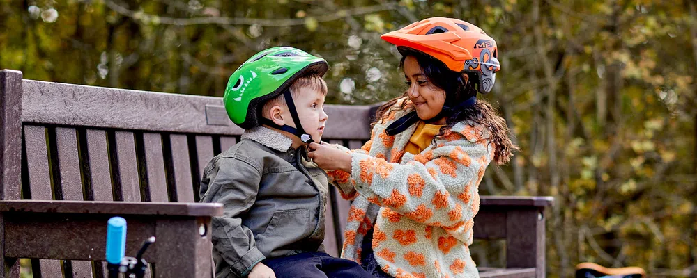 one child helping another to put on a bike helmet for cycling