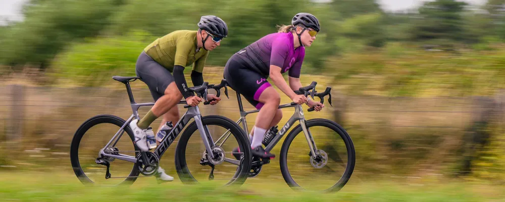 man and woman riding performance road bikes by Giant and Liv quickly on closed road circuit - pan shot