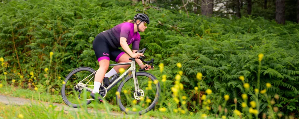 Woman riding a performance road bike in purple Liv kit with yellow flowers in the foreground