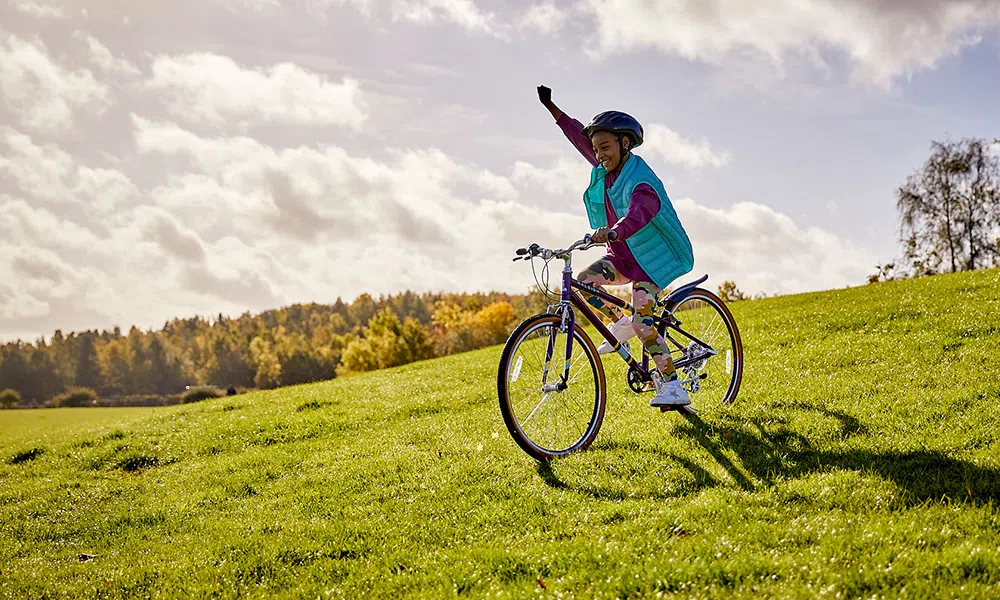 Girl riding a junior bike down a grassy bank with hand in the air