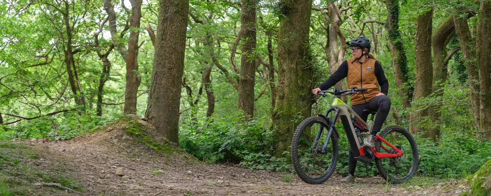 Woman standing in the woods on a sunny day astride a Cannondale eMTB wearing Troy Lee Designs cycling clothing