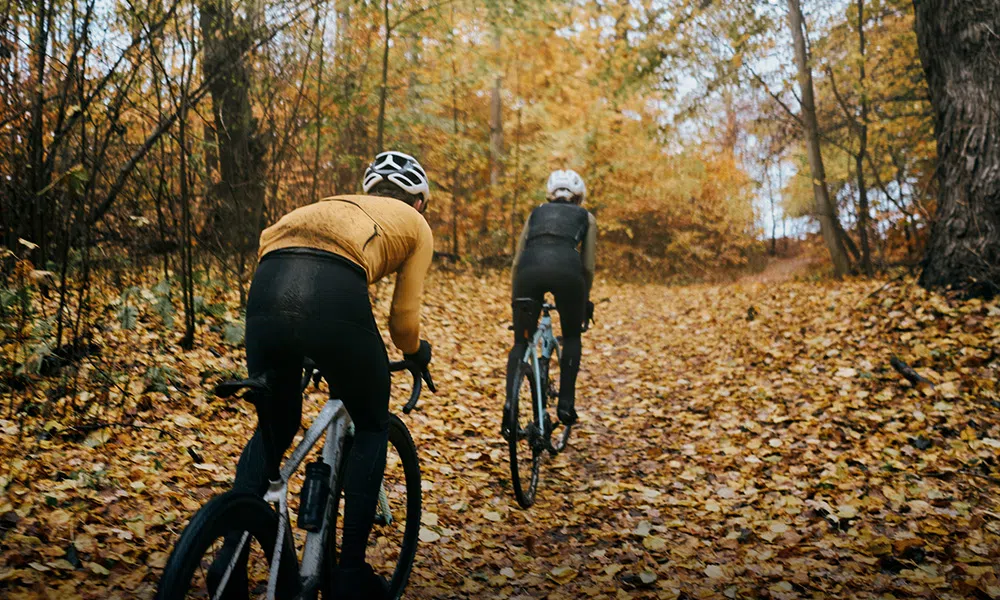 Two gravel riders cycling through autumn leaves