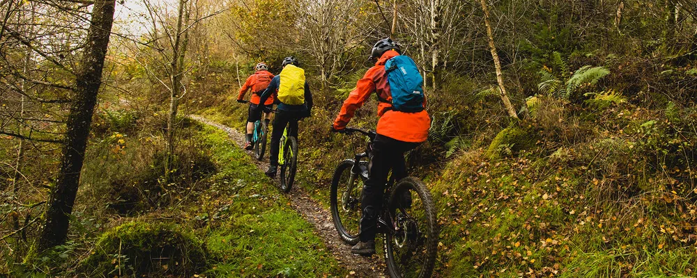 3 mountain bikers riding uphill with hydration packs