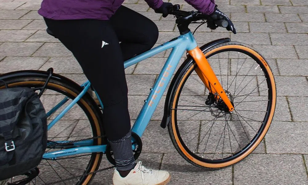 riding a hybrid e-bike with mudguards and pannier bag close up