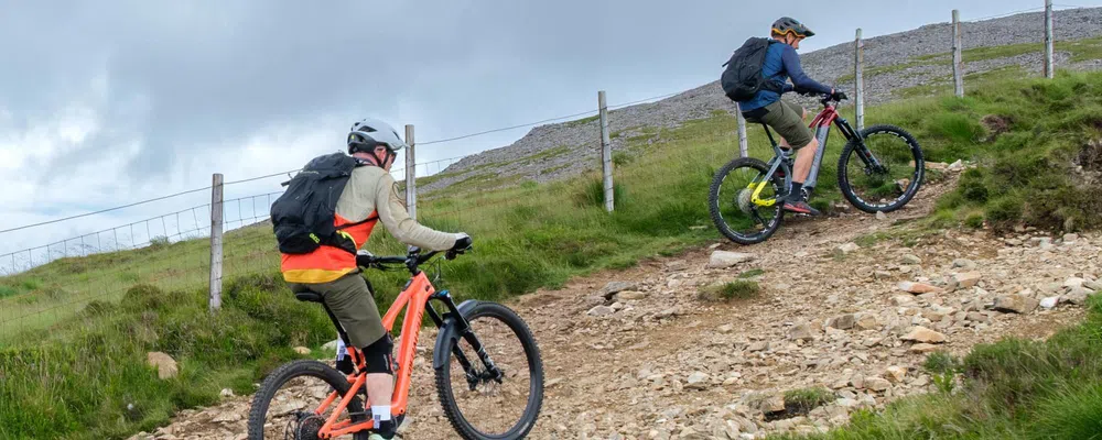 two cyclists riding uphill on a rough gravel track on e-MTBs