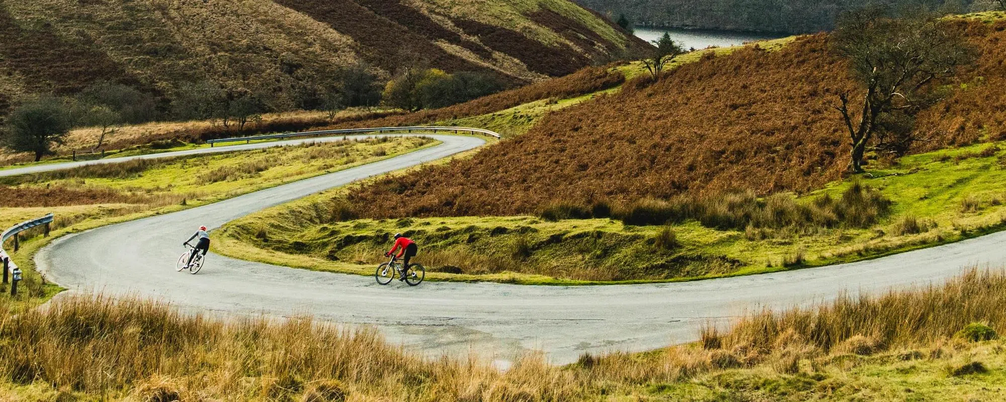 Two road cyclists descending on a winding road on an autumn day in the Welsh hills