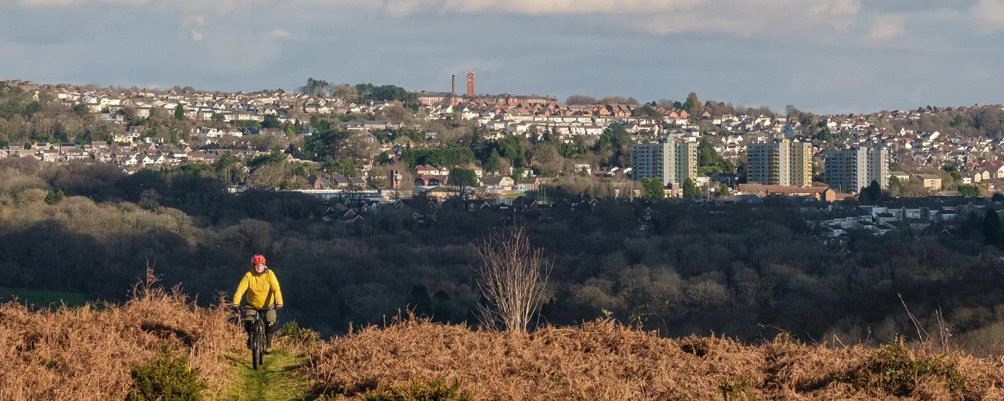 mountain biker riding up a grassy track with city in the background