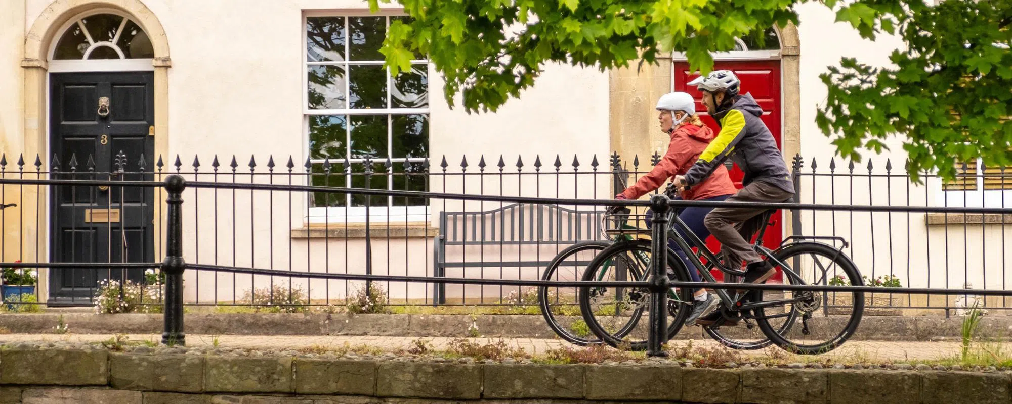 two cyclists riding along an urban path past houses