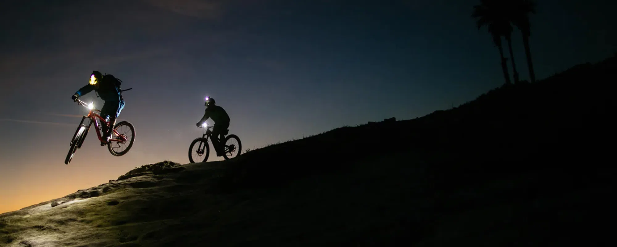 two mountain bikers at sunset using exposure lights