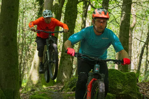 two mountain bikers riding in the woods on a warm sunny day