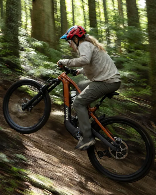 Woman riding a Trek eMTB up a steep climb in the woods