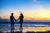 a couple walking down a beach holding hands during a sunset