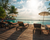 an infinity pool facing the sea bordered by a deck with sunbeds on it 