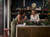 Two female friends laughing, drinking coffee and sharing a phone screen at a kitchen island