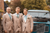 A groom and groomsmen in beige suits pose next to a vintage Land Rover car