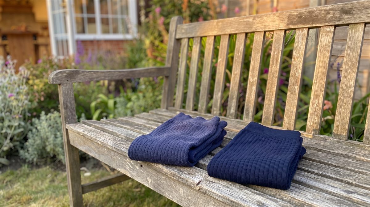 An older pair and a newer pair of navy compression socks side by side on a weathered garden bench