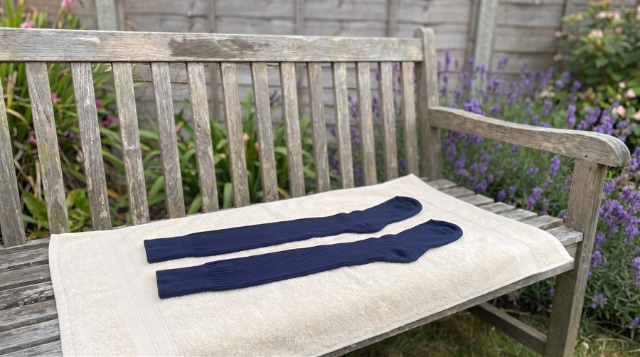 A pair of compression socks laid flat on a clean towel on a bench, drying in the shade