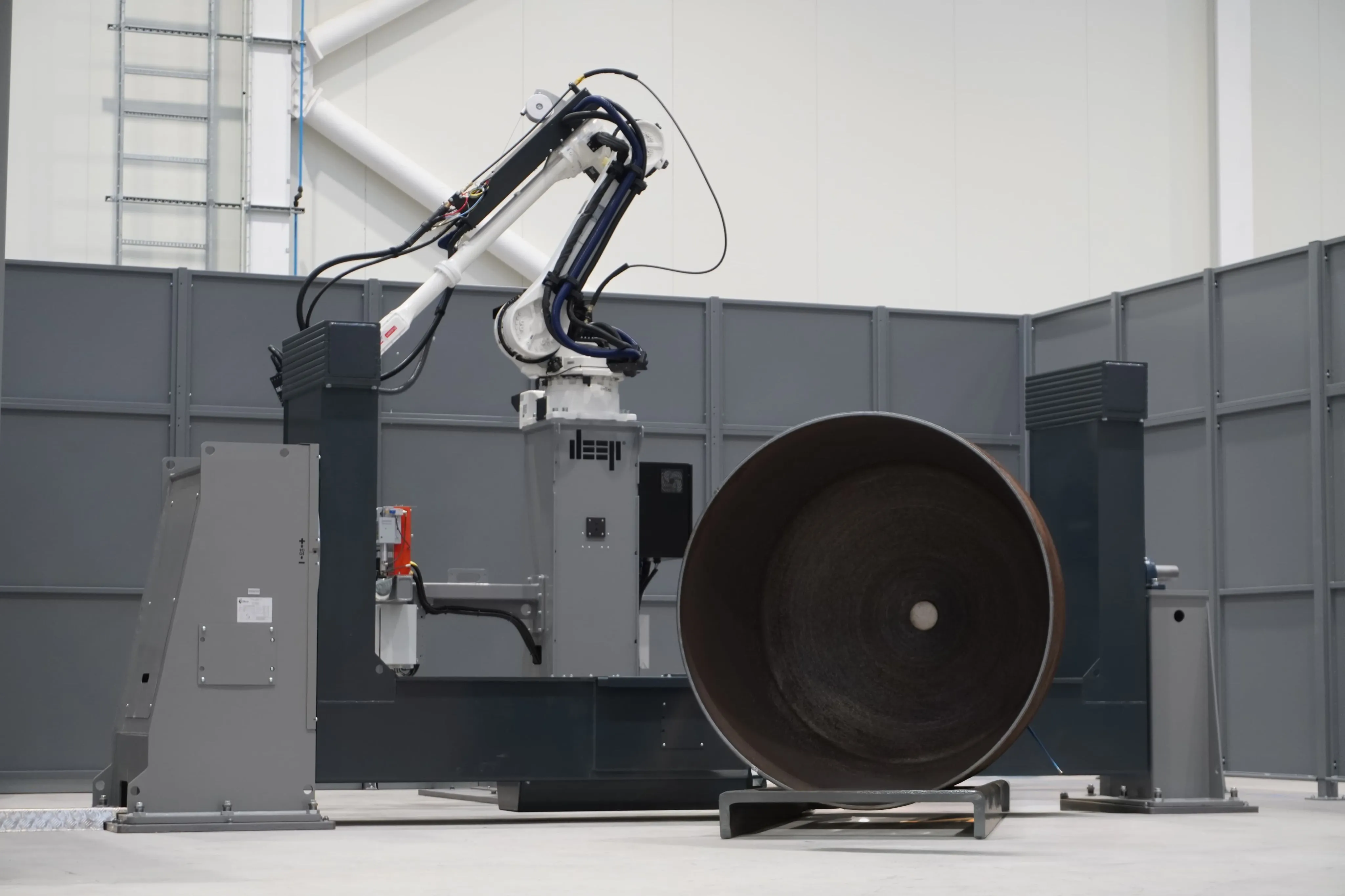 A two axis manipulator WAAM robot with a metal printed hemisphere next to it.
