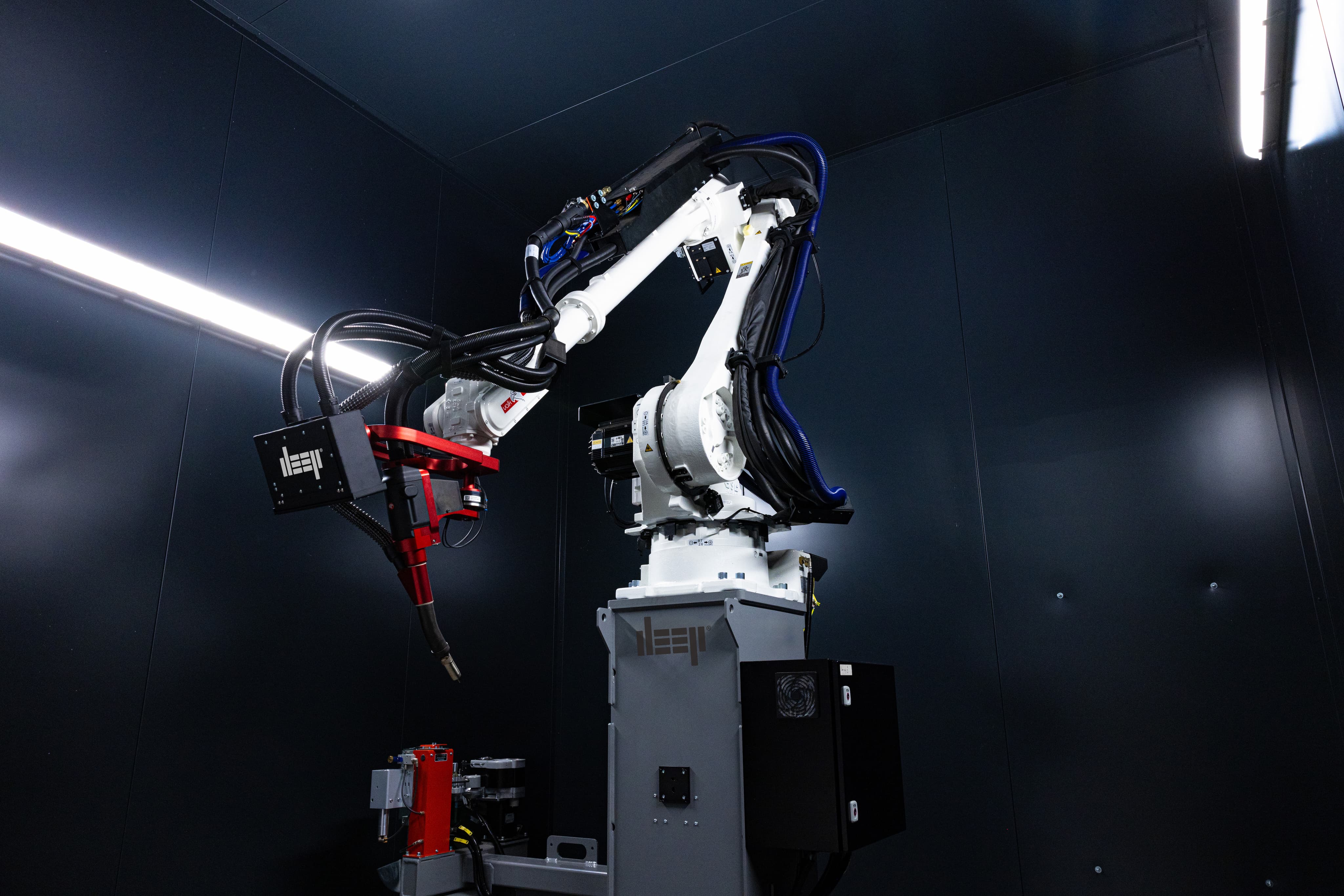 An image of a WAAM robot in a dark enclosed cell.