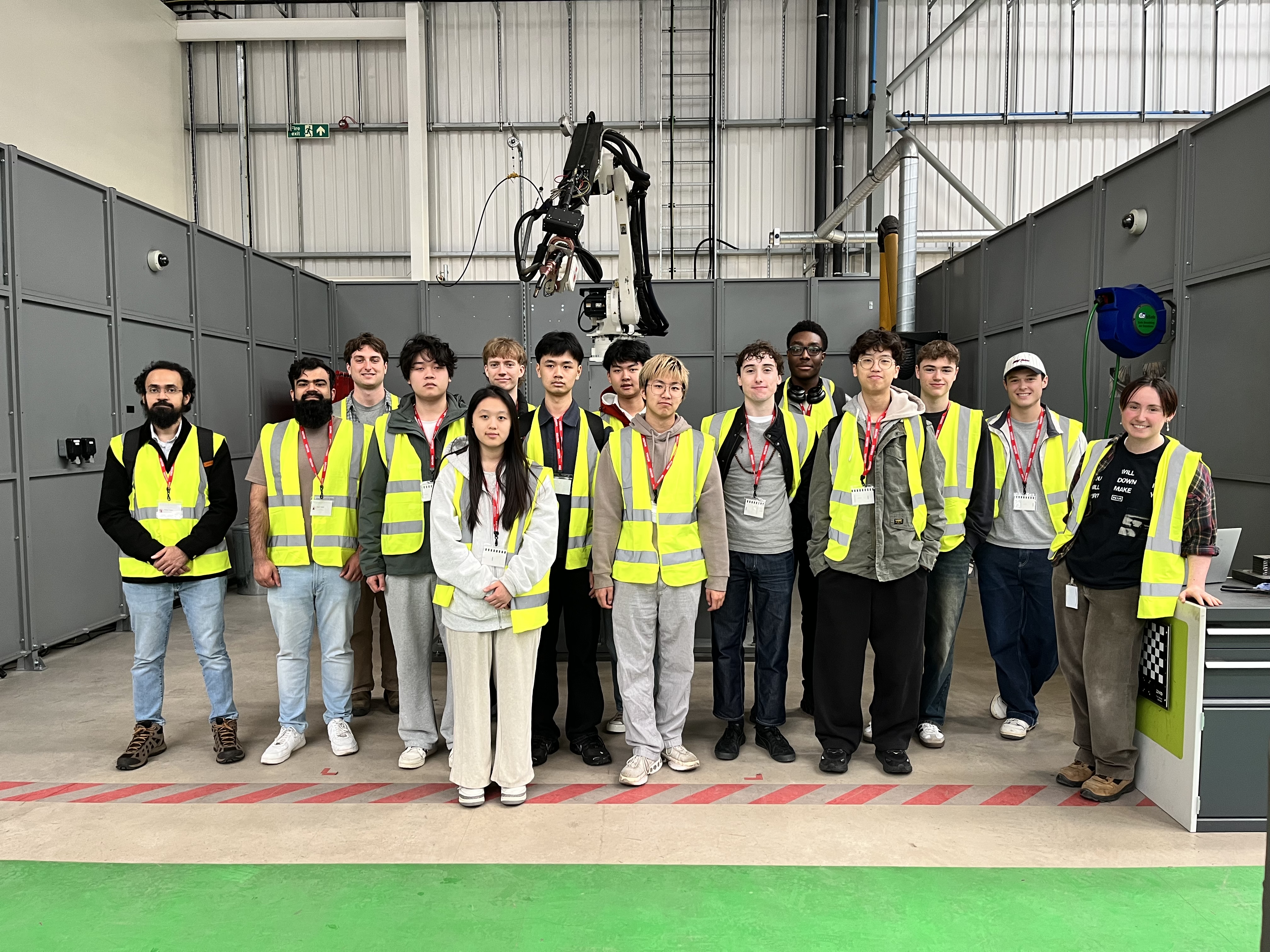 Several people high-vis jackets standing in front of a WAAM robot