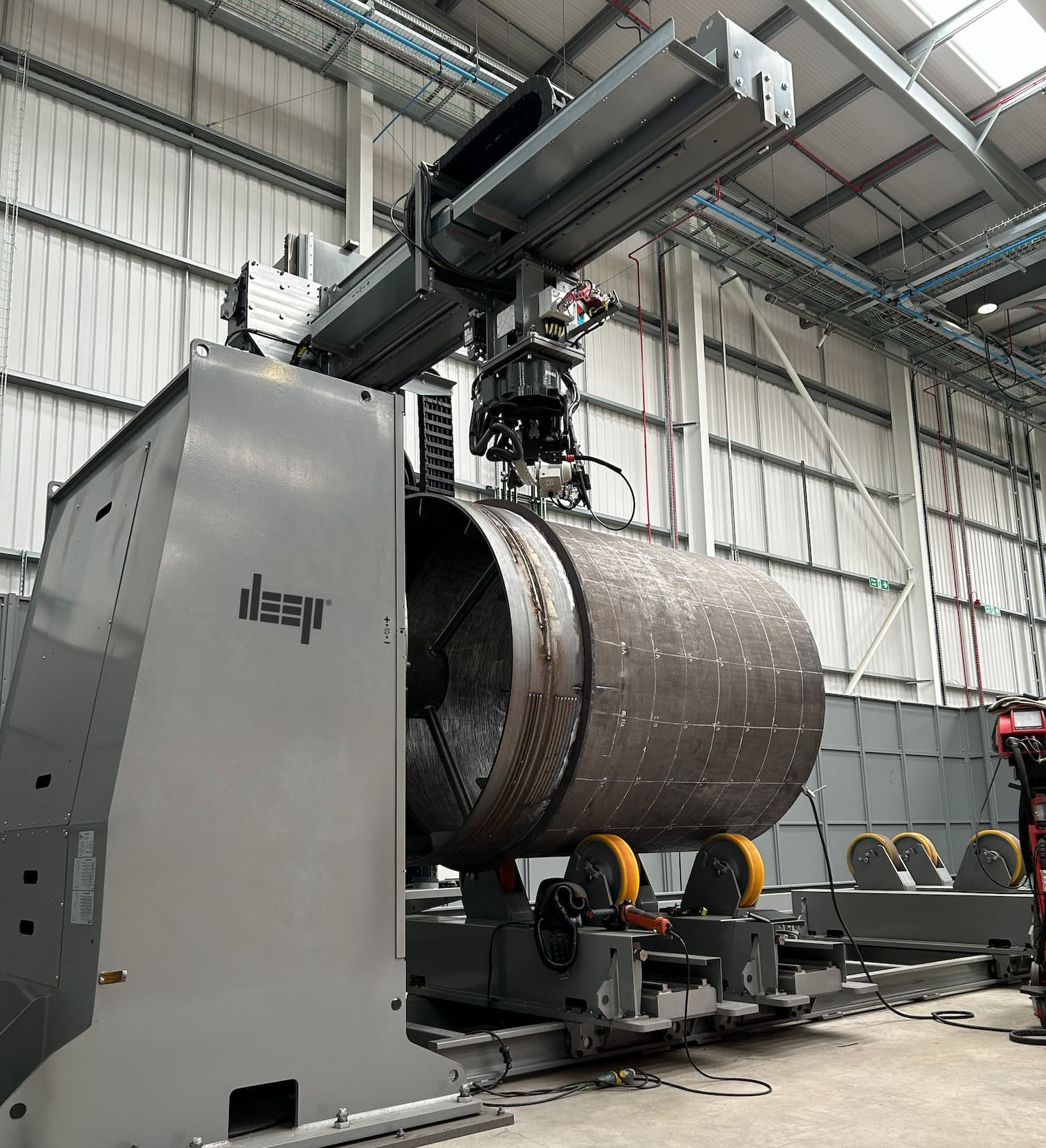 A large metal cylinder mounted on a gantry system in a manufacturing warehouse.